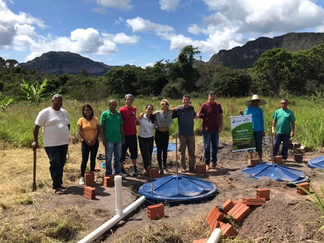Grupo reunido durante visita a uma fossa ecológica com serras ao fundo